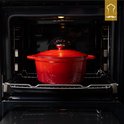 Rode gietijzeren pan met deksel in een open oven.