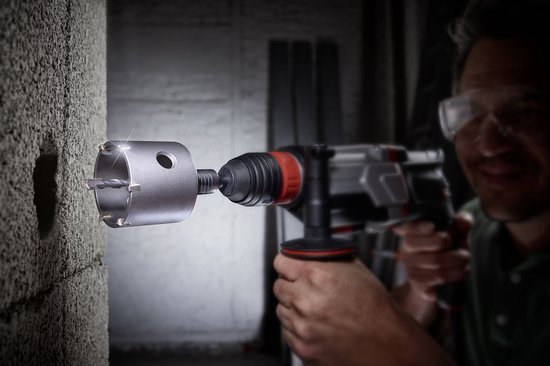 Een man met veiligheidsbril boort met een grote, metalen boor met rode accenten in een betonnen muur.