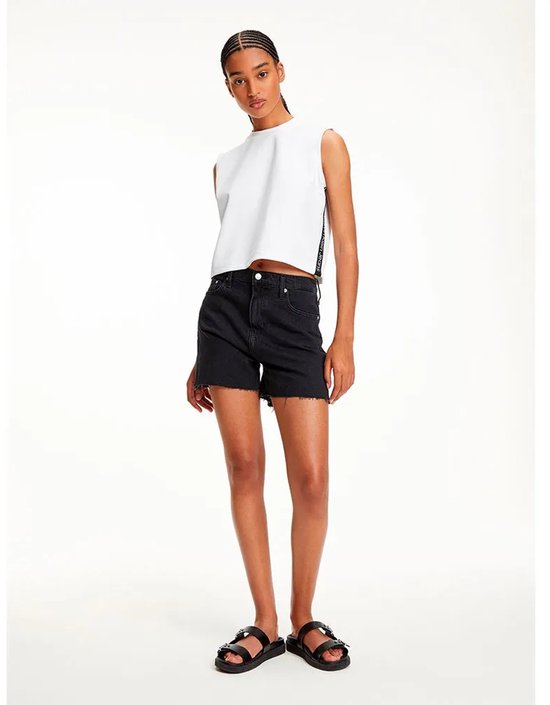 Model in wit mouwloos T-shirt met Calvin Klein Jeans logo tape aan de zijkant, gecombineerd met zwarte denim shorts.