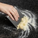 Roestvrijstalen deegschraper veegt deegkruimels van een donker aanrecht.
