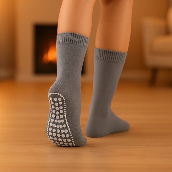 Een persoon die grijze huissokken met witte antislip noppen draagt, bij een open haard.
