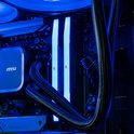 Close-up van de binnenkant van een gaming pc met blauw verlicht RAM-geheugen en een waterkoelingsysteem met zwarte slangen.