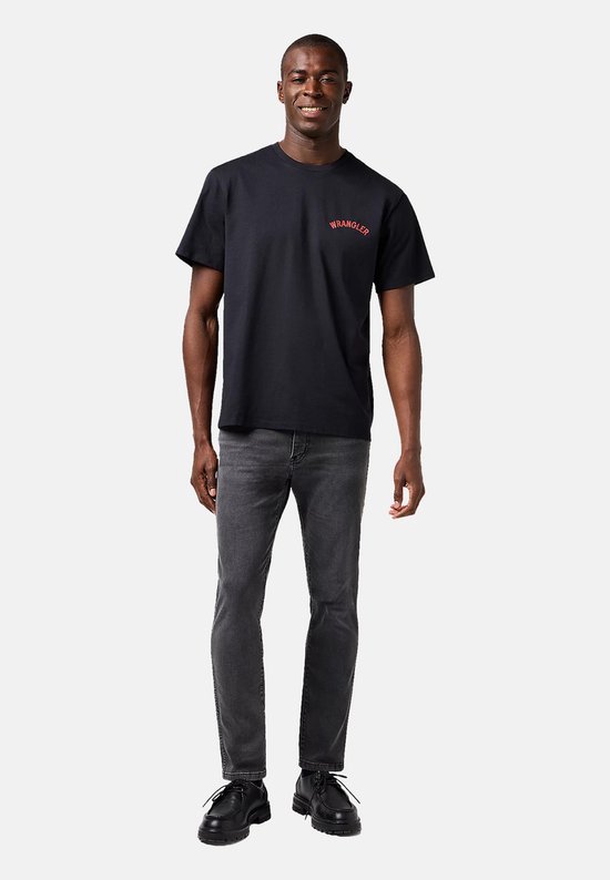 Man met donkere huid, draagt een zwarte t-shirt en grijze spijkerbroek.