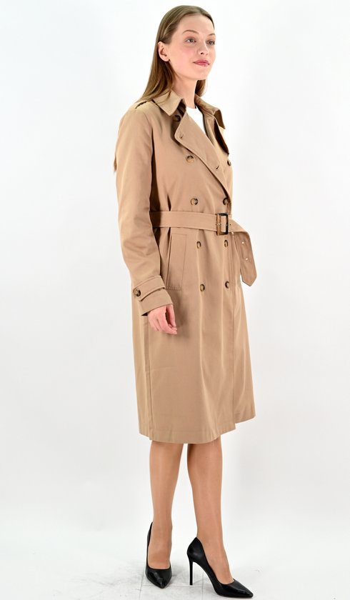 Model in camelkleurige lange trenchcoat met ceintuur, linkerhand in de zak.