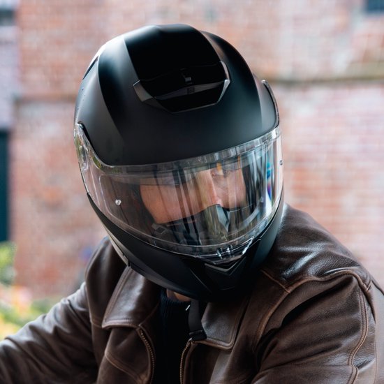 Close-up van een matzwarte systeemhelm met getint vizier, gedragen door een man met bruine leren jas.