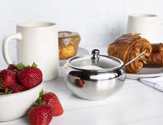 Glanzende RVS suikerpot met glazen deksel, naast verse aardbeien en mokken.
