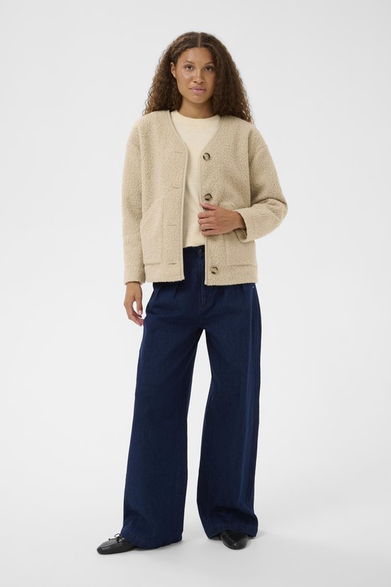 Model draagt een beige teddy jas met knopen en een beige trui. Verder een donkerblauwe wijde jeans.