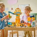Kinderen spelen met geel bouwspeelgoed met kraan, vrachtwagen en betonmixer.