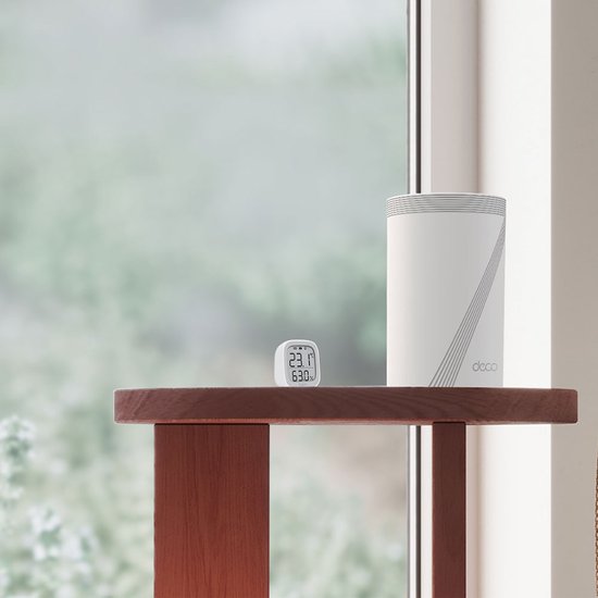 Witte Deco BE65 router met grijze lijnen, naast een kleine digitale thermometer op een houten tafel.
