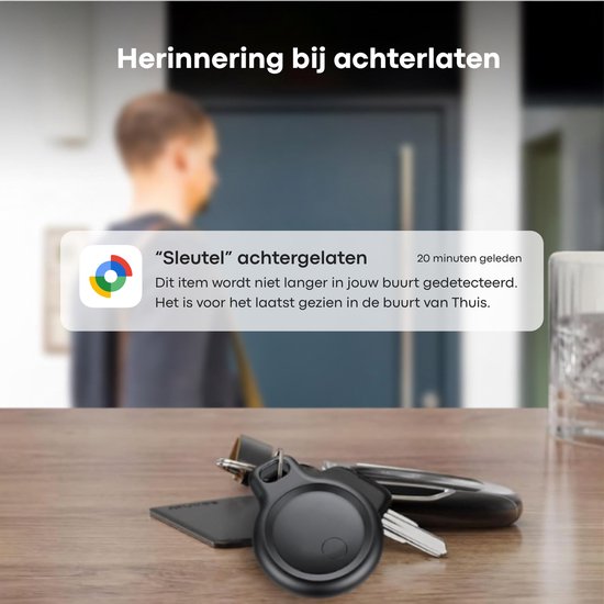 Een zwarte ronde tracker met sleutelring op een houten tafel, met een notificatie 'Sleutel achtergelaten'.
