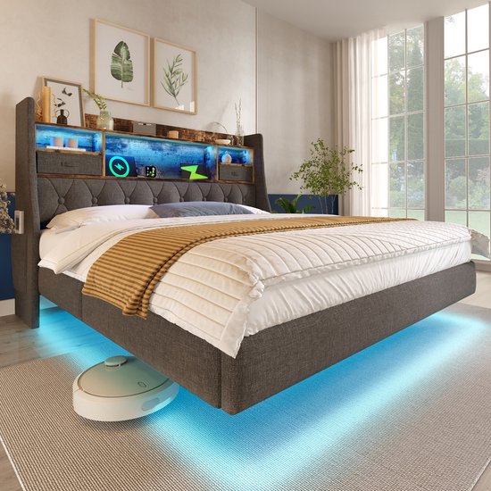 Grijs gestoffeerd bed met zwevend design, hoofdeinde met opbergvakken en blauwe LED-verlichting, bij een raam. Getoond met de tekst 'APP + Fernbedienung LED'.
