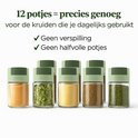 Zes glazen kruidenpotjes met groene deksels, gevuld met specerijen zoals kardemompeulen en mungbonen.