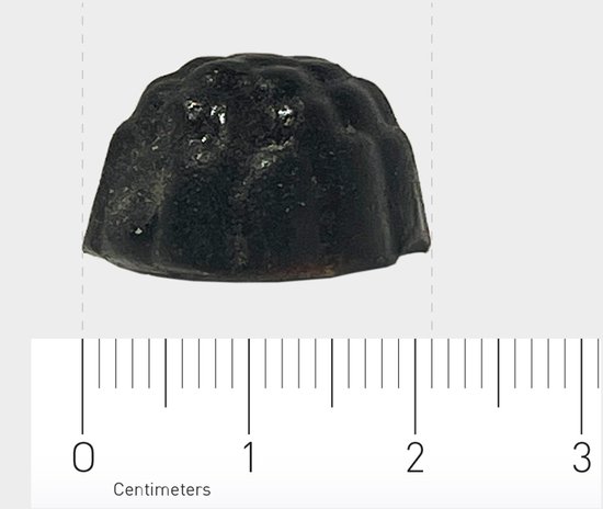 Eén donkere, ronde gummy met geribbelde zijkanten, naast een centimetermaat.