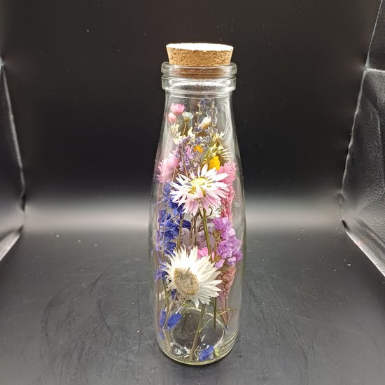 Glazen fles met kurk, gevuld met gedroogde bloemen in roze, paars, wit en blauw.