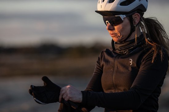 Vrouw met een helm en zonnebril, die zwarte handschoenen aantrekt.
