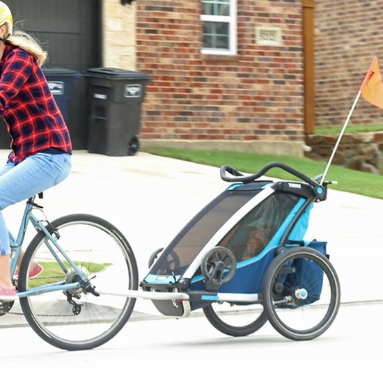 Zijkant van een blauwe fietskar met wielen, met een oranje vlag.