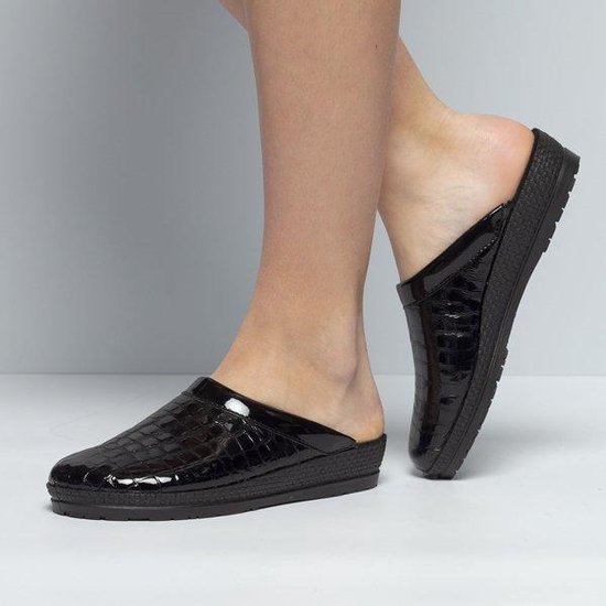 Een paar zwarte glanzende pantoffels met krokodillenprint, gedragen door een vrouw op haar voeten.