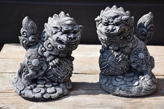 Twee grijze stenen foo dog tuinbeelden, zittend op sokkels met wolkenmotief.