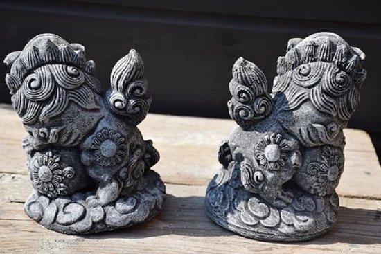 Twee grijze stenen foo dog tuinbeelden, zittend met bloemenmotief op lichaam, van achteren.