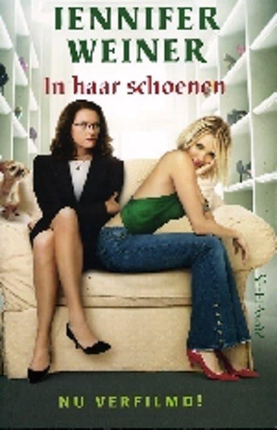 Twee vrouwen, met een bril en in pak, en blond met groene top, zitten op een bank met schoenen op de achtergrond.