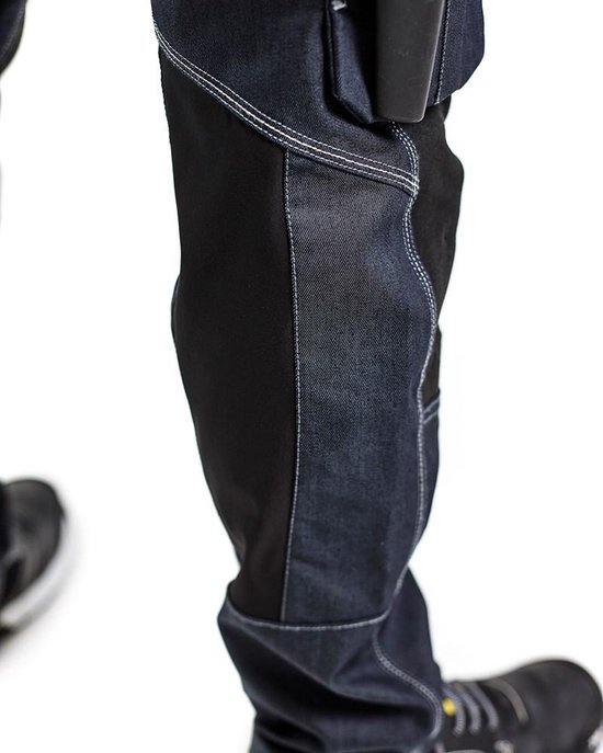 Detail van de onderkant van een werkjeans, met donkerblauwe denim en zwart verstevigd materiaal.