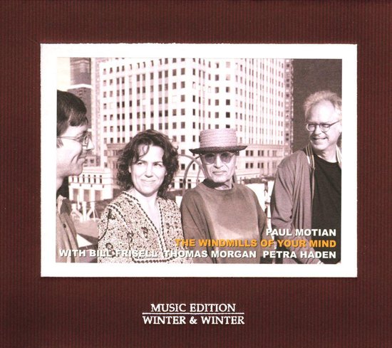 Portretfoto van vier muzikanten, waaronder een vrouw met een patroonvest. Op de achtergrond gebouwen. Titel: 'The Windmills of Your Mind'.
