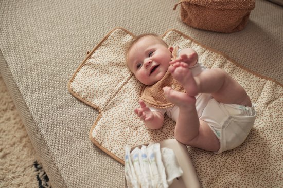 Baby ligt op een luierwisselhoes met luierdoekjes in een hoesje ernaast, met een speentje.