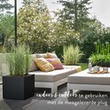 Een stijlvolle tuinmeubellounge met comfortabele kussens en een zwarte plantenbak met gras.