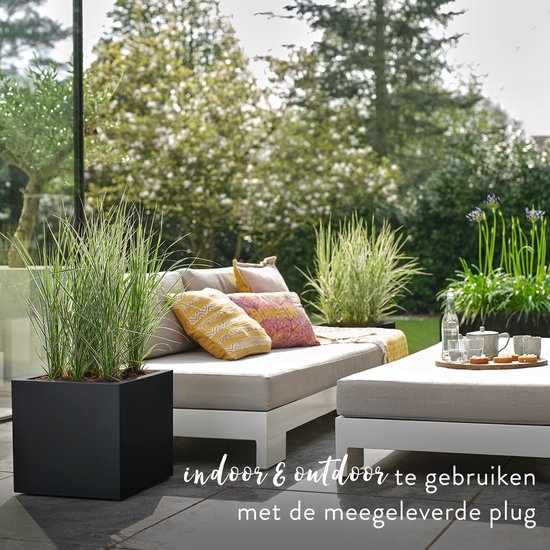 Een stijlvolle tuinmeubellounge met comfortabele kussens en een zwarte plantenbak met gras.