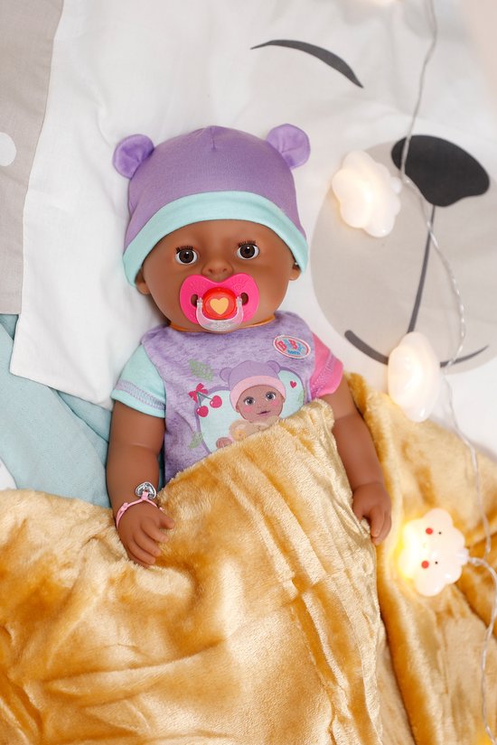 BABY born Eva pop met paarse muts en paarse bodysuit met berenprint, liggend in bed met speen en deken.