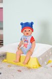 BABY born pop met blauwe muts en romper met beerprint. Zittend op een geel plateau.