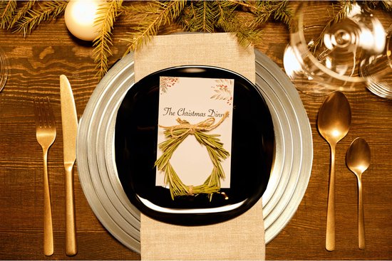 Gouden bestek op een gedekte tafel met zwarte borden en een kerstkaart.
