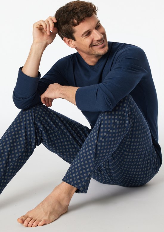 Man zit ontspannen op de grond, draagt een donkerblauwe pyjamaset.