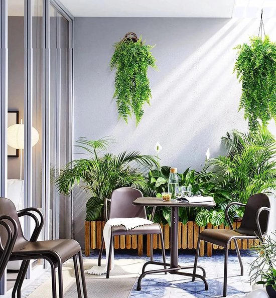 Twee groene kunsthangplanten sieren een balkon met een tafel en stoelen.