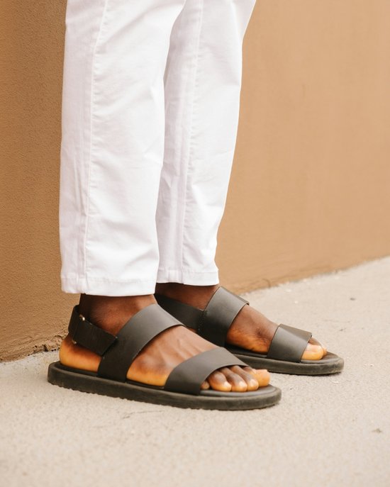 Donkergroene sandalen met twee banden en een gesp, gedragen door een persoon met een witte broek.