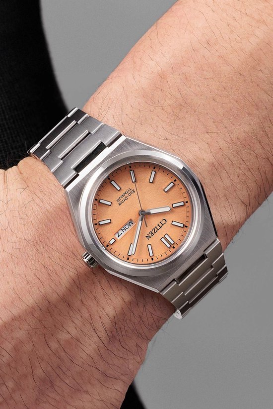 Citizen Eco-Drive horloge met perzikkleurige wijzerplaat, gedragen op een mannelijke pols.