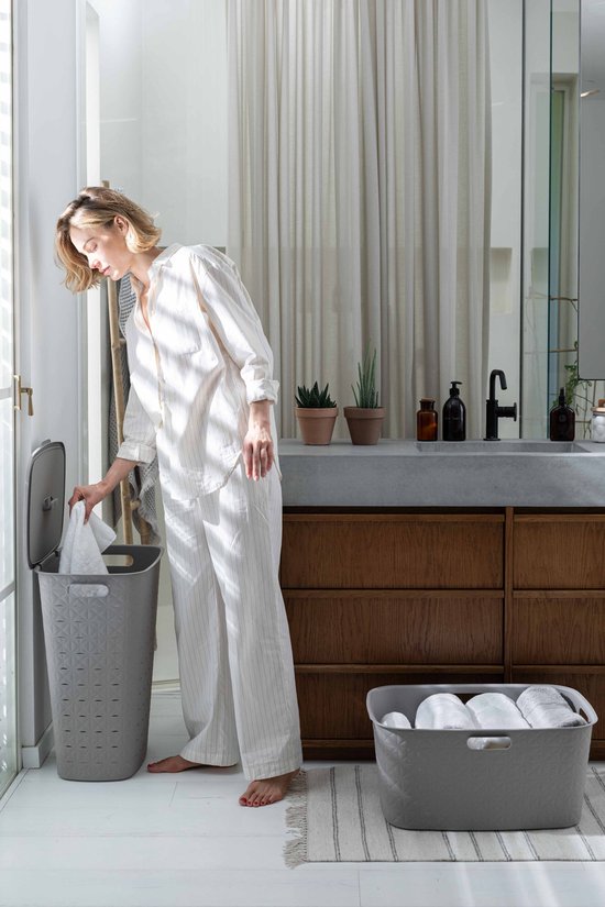 Vrouw in gestreept pyjama met grijze wasmand met deksel, op de achtergrond een grijze wasmand.