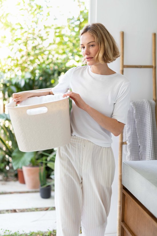 Vrouw met kort blond haar houdt een beige wasmand met ruitpatroon vast.