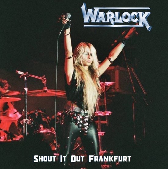 Zangeres met lang blond haar in een zwart korset, leren broek en met haar armen omhoog, met het Warlock logo erboven. Tekst: SHOUT IT OUT FRANKFURT