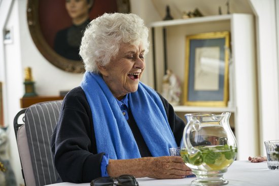 Dame Eileen Atkins lacht en houdt een glas vast, met een blauwe sjaal om haar nek.