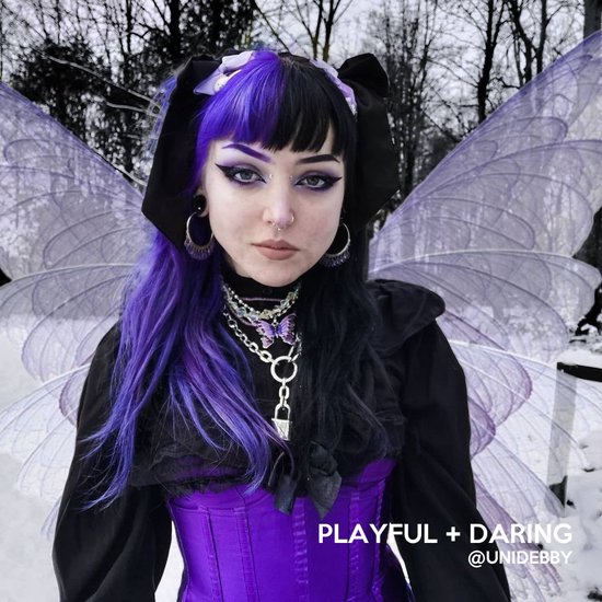 Model met half zwart, half paars haar, met vleugels en paarse korset. Tekst "PLAYFUL + DARING".