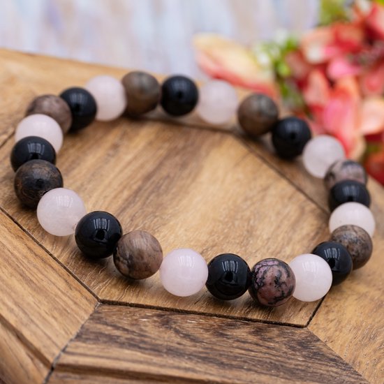 Armband met roze, zwarte en bruine kralen op een houten achtergrond.