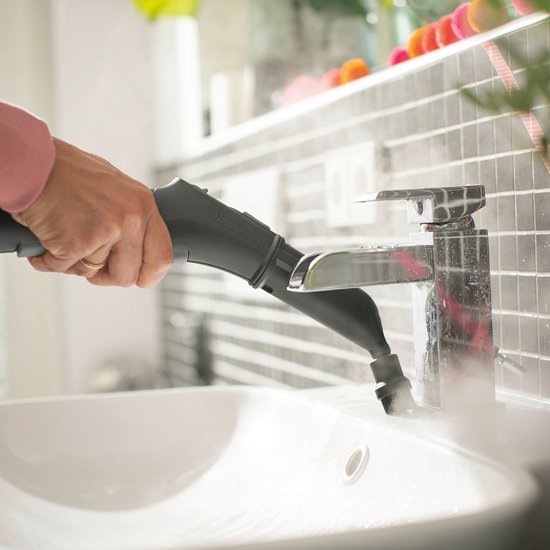 Main tenant un nettoyeur vapeur et nettoyant un robinet au-dessus d'un lavabo blanc.