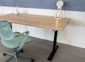Houten bureau met zwart frame, naast een groene bureaustoel.
