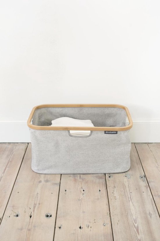 Grijze Brabantia wasmand met bamboe frame, gevuld met witte handdoeken.