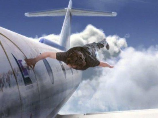 Man valt naar beneden, zijn hand grijpt naar een vliegtuig in de lucht.
