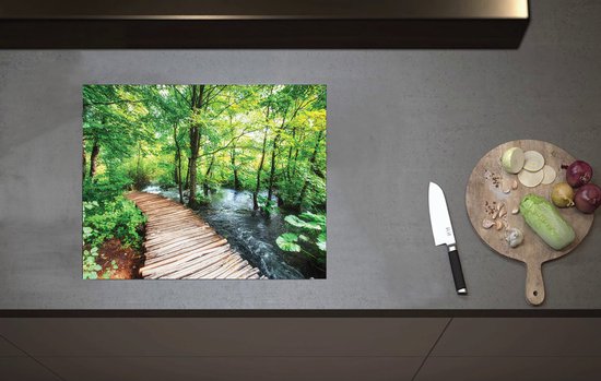 Inductiebeschermer met houten vlonderpad door groen bos en rivier op een grijs aanrecht met een snijplank en mes.