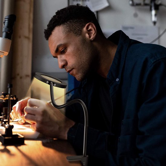 Man met vergrootglas met LED-verlichting, geconcentreerd aan werk