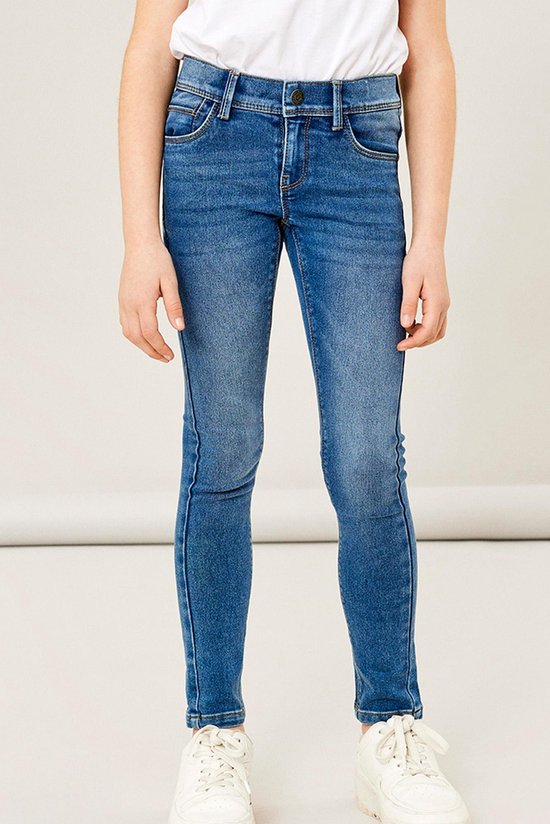 Meisje in een spijkerbroek met skinny fit in medium blauwe denim, met de handen op de zakken.