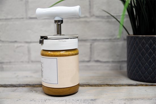 Een pot pindakaas met een witte potopener erop, op een houten tafel.